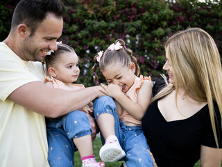 Familiy portrait at the park where dad tickles one of his daughters. They all smile and laugh.
