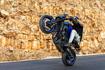 A motorcycle racer performs a difficult and dangerous stunt on his motorcycle. Riding on the back...