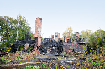 Burnt ruins of a collapsed house with charred remains and tall chimneys surrounded by nature