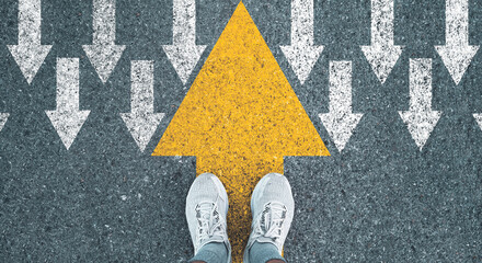 Man standing on yellow big arrow opposite  direction with white arrow on road asphalt for different...