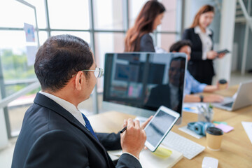 Asian senior businessman working on a digital tablet in a modern office environment, utilizing technology to manage corporate tasks, enhance productivity, and communicate with team members effectively