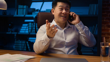 Happy Asian man worker manager executive boss entrepreneur at night office talking mobile phone at...