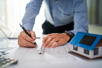 A man is drawing a house on a piece of paper. He is wearing a blue shirt and glasses