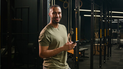African American fitness man athlete sport trainer smiling laughing reading funny news watching humorous video joke in smartphone sportsman browsing mobile phone laugh looking at camera smile in gym