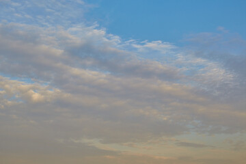 Delicate yellow rays of the setting sun on blue clouds, pastel colors of the evening sky, celestial landscape with sunset clouds.