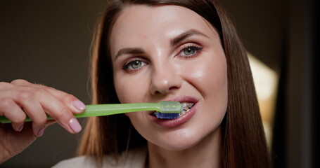 Young woman with braces brushing teeth with green toothbrush. Close-up of dental hygiene routine,...