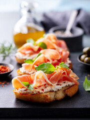 Bruschetta, crostini, toasts with cream cheese, Jam?n, ham and fresh basil on dark marble board. Close up.
