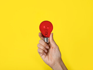Woman holding red light bulb on yellow background, closeup