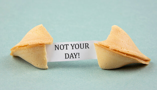 Opened fortune cookie with a piece of paper inside, a "fortune" saying: NOT YOUR DAY! Sarcastic bad luck concept. Blue color studio background.