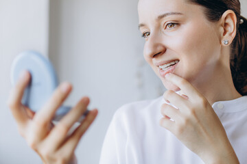 Young Woman Is Checking Her Teeth For Imperfections In A Small Mirror. New Technology For Teeth Straightening. Dental Health Medical Care Concept.