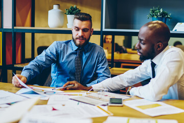 Multicultural business colleagues in shirts communicating with each other about financial reports on documents during business meeting in office.Partnership of leaders during working process
