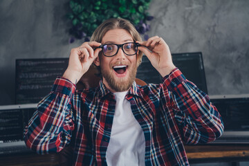 Portrait of handsome bearded young man wearing checkered shirt touching glasses shocked near his...