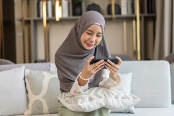 Asian muslim woman use smartphone at home, female in hijab checking messages, modern communication, smiling and holding mobile device technology use, staying connected, lifestyle concept, social media