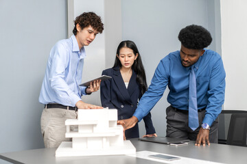 Architects engineers collaborating on building design project in modern office, diverse team of professionals female muslim architect and male engineers discussing architectural model of structure