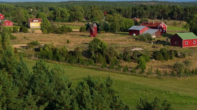 Aerial views capture traditional red farm buildings and a windmill amidst vibrant green and yellow fields in Aland, Finland, showcasing the region's picturesque rural scenery