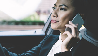 Fototapeta premium Professional female driver concentrated on road trip in automobile making international call conversation with colleague for discussing time of business meeting, woman trader using smartphone gadget
