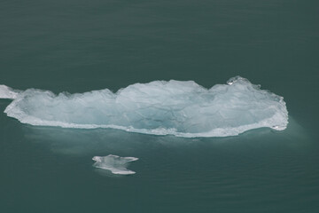 Glacial Ice floating up close in open waters, surrounded by blue green calm, cooling waters.
