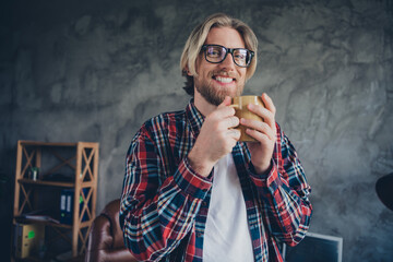 Portrait photo of young blond hair man cheerful office manager holding cup warm tea having coffee break indoors loft design modern office