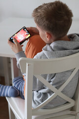 Teenage boy sitting on a chair at home and playing a game on his smartphone