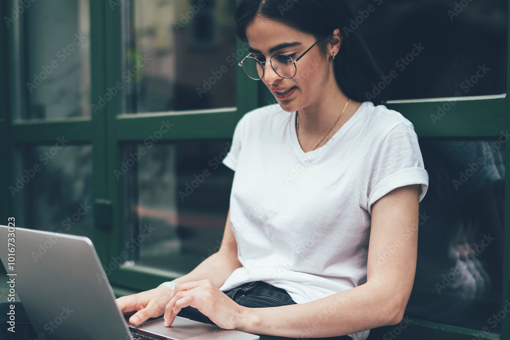 Poster serious hipster programmer in optical eyewear working online with startup sitting at urban near city