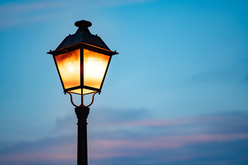 Evening street lamp illuminated with tree branches in the foreground under a twilight sky, creating a peaceful and tranquil mood.