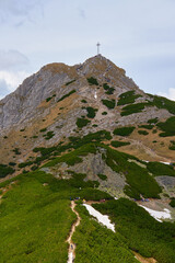 Fototapeta premium Rugged hiking trail leading to mountain summit with large cross under cloudy sky. Tatra mountains in Zakopane, Poland. Giewont mountain summit. Natural landscape