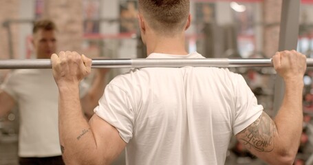 Fototapeta premium Back and leg workout with weighted squats man is seen from behind, lifting weights in a gym. Emphasis on fitness and strength training