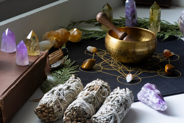 A close up image of a brass meditation singing bowl on a crystal grid with healing crystals and sage smudge sticks. 