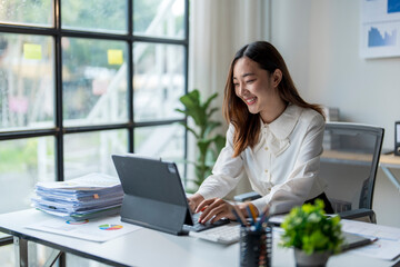 Young asian businesswoman working on a digital tablet and smiling at the office