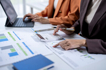 Businesswomen analyzing financial charts and using calculator in office meeting