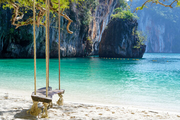Sea view from sand beach at seashore with a wooden board swing hanging from branch of tree by nylon...