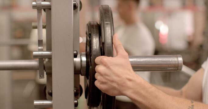 Remove the weight from the bar with your hands. Man preparation for a workout session, enthusiast is enhancing gym equipment with added weights