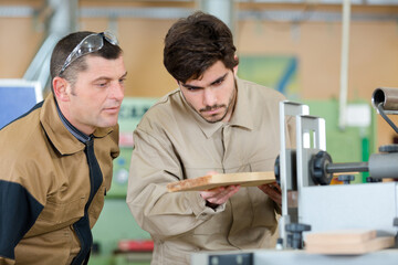 carpenter working with apprentice in industrial tool in wood factory