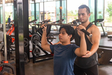 Male Trainer Assisting trainee to do the correct exercise postures in Large Fitness Center Filled with Workout Equipment