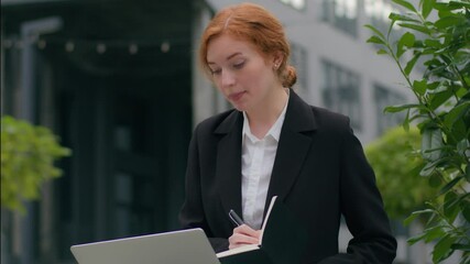 Young Caucasian businesswoman female girl business woman student working online consult client using app talking video call laptop pc device speak conference meeting writing notes outside city office