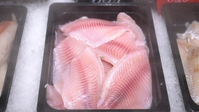 A fresh tilapia fish fillet lies on an icy counter in a store under a cooling spray