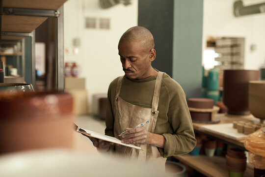 African potter taking inventory of pots on shelves in a ceramics workshop