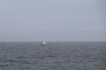 Obraz premium Lone sailboat on a vast empty ocean in misty conditions