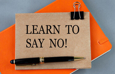 LEARN TO SAY NO! - words on paper on a gray background. Notebook and pen in the background
