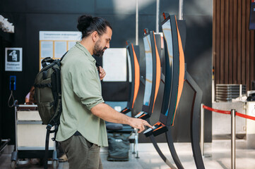 A man checks in for a plane at the electronic check-in desk. A young tourist guy at the airport...