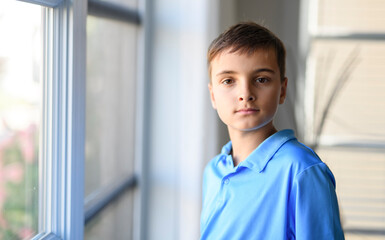 young teenager boy with close to the window at home