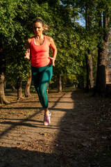 Beautiful woman running in park. Beautiful adult woman is jogging outdoor on sunny day in autumn. Woman running for health and wellness in the morning sunrise at park.