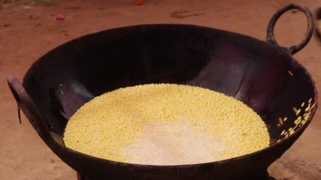 Bundi batter is poured through a perforated ladle into hot oil in a large kadhai for frying, creating a traditional Rajasthani sweet.