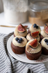 Chocolate cupcakes with cream cheese frosting, fig slices, blueberry and cocoa powder.
