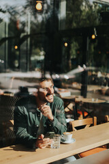 Toughtful man savoring coffee alone at a cozy cafe on a sunny day while lost in contemplation by the window