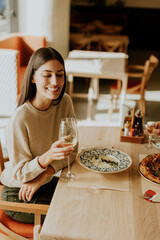 A joyful woman enjoying a glass of white wine while dining on a delicious meal at a trendy restaurant in the heart of the city
