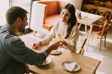 Couple enjoying refreshing cocktails at a cozy cafe in the afternoon sunlight while savoring delightful snacks together