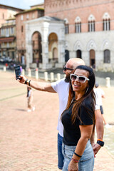 Fototapeta premium Happy smiling couple of tourists walking at Piazza del Campo at Siena. Concept of Italian gastronomy and travel. Italian couple having aperitivo together