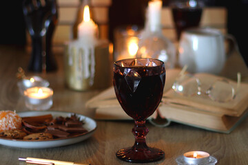 Books, lit candles, red wine, snacks and various deocration on the table. Dark academia or Halloween concept. Selective focus.