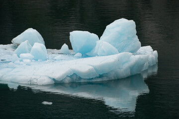 Front lip of a floating iceberg comprised of glacial blue ice with other cute chunky ice blocks above along for the ride.